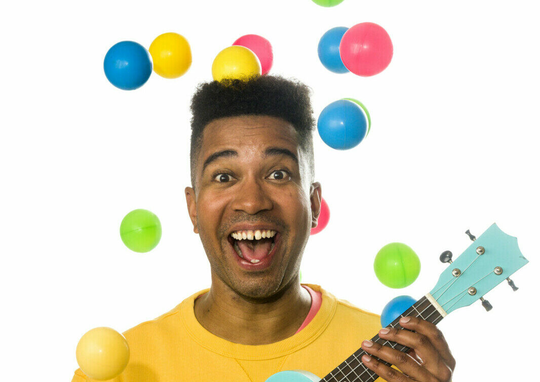 Yankho ler och håller en Ukulele, färglada bollar som faller runt honom